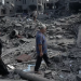 Warga Gaza melewati puing-puing bangunan yang runtuh dihantam rudal zionis Israel. (EPA)